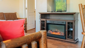 A living room with a fireplace, a television mounted above it, and a wooden chair in the foreground. - Newly Renovated, Waterfront Cottages located in Prince Edward County (Milford)