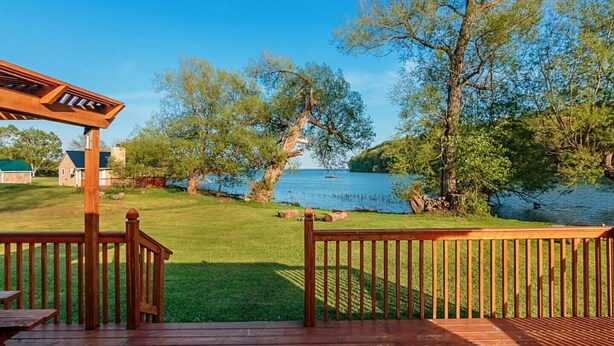A deck with a view of a lake, surrounded by trees and a grassy area. - Newly Renovated, Waterfront Cottages located in Prince Edward County (Milford)