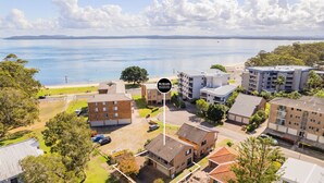Oversigtsbillede af Nelson Bay Accommodation med udsigt til stranden, flere bygninger og en parkeringsplads.