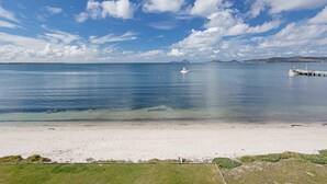 A beach with clear water, a boat, and a distant island. - 2/137 Soldiers Point Road - luxury unit on the waterfront with aircon and free unlimited WiFi (Soldiers Point)