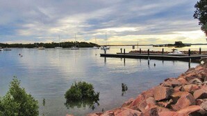 A calm lake with boats docked at a pier, surrounded by rocky shores and trees. - 2/137 Soldiers Point Road - luxury unit on the waterfront with aircon and free unlimited WiFi (Soldiers Point)