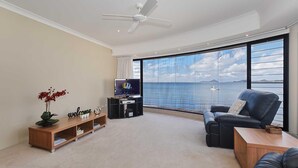 A modern living room with a large window offering a sea view, a flat-screen TV, a leather sofa, and a wooden entertainment unit. - 2/137 Soldiers Point Road - luxury unit on the waterfront with aircon and free unlimited WiFi (Soldiers Point)
