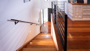 Un escalier avec une finition en bois, une rampe noire et un mur blanc avec une porte en haut.