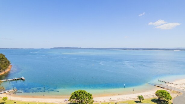 A coastal view with clear waters, a sandy beach, and a pier extending into the sea. - Mistral Court, 14/17 Mistral Close - across the road from the beach (Nelson Bay)