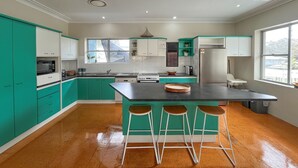 Une cuisine moderne avec des armoires de couleur turquoise, un îlot central doté de tabourets et une vue sur l’extérieur grâce à de grandes fenêtres.