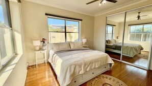 Une chambre à coucher avec un lit, des tables de chevet, un miroir et une vue sur l’extérieur.