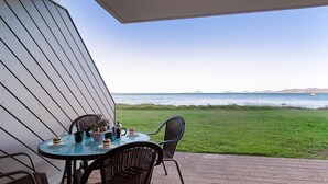 Un patio con mesa y sillas que da a un área verde y al mar.
