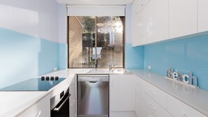Una cocina moderna con lavavajillas integrado, estufa a gas y ventana con vista a un muro de ladrillo y follaje exterior.