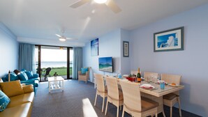 Una habitación con vista al mar, un comedor con sillas de mimbre, un sofá con cojines azules y un ventilador de techo.