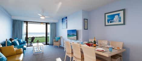 Ein Zimmer mit Meerblick, ein Essbereich mit Korbstühlen, eine Couch mit blauen Kissen und ein Deckenventilator.