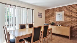 Ein Essbereich mit Holztisch und Stühlen, einer Ziegelwand und einem Fenster mit Jalousien.
