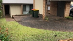 Ein Einfahrt mit Garage, einer grünen Mülltonne und einer kleinen Rasenfläche.