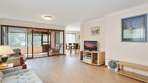 Ein modernes Wohnzimmer mit Flachbildfernseher, einer Couch, einem Essbereich und einer Schiebetür zu einem Außenbereich.
