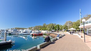 A marina with boats docked, a couple sitting on a bench, and a building with outdoor seating. - Yarramundi, 4,47 Magnus Street - air conditioned unit with air con, wi-fi, water views and close to town (Nelson Bay)
