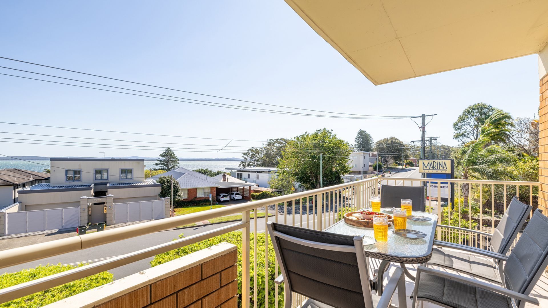 A balcony with a table and chairs, overlooking a residential area with houses and a marina sign.
