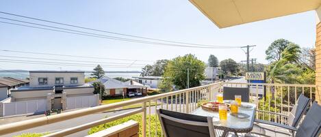 A balcony with a table and chairs, overlooking a residential area with houses and a marina sign.