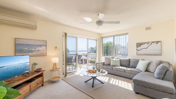 A living room with a television, sofa, coffee table, and a view of the outdoors. - Yarramundi, 4,47 Magnus Street - air conditioned unit with air con, wi-fi, water views and close to town (Nelson Bay)