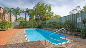 A rectangular swimming pool with a metal ladder, surrounded by a pebble path and greenery, with a building and a green fence in the background. - The Point, 5, 5-7 Mitchell Street large balcony with great water views (Soldiers Point)