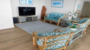 A living room with a flat-screen TV, wicker furniture, and a large rug. - The Point, 5, 5-7 Mitchell Street large balcony with great water views (Soldiers Point)