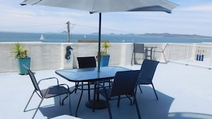 A rooftop terrace with a table and chairs, potted plants, and a view of the sea and distant hills. - The Point, 5, 5-7 Mitchell Street large balcony with great water views (Soldiers Point)