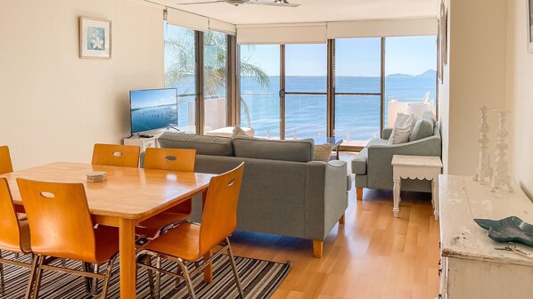 Un vaste espace de vie doté d’une grande fenêtre donnant sur la mer, d’une table à manger avec des chaises et d’un canapé.