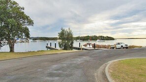 Un espace de stationnement au bord de l’eau, avec une route asphaltée, un quai et un bateau en arrière-plan.