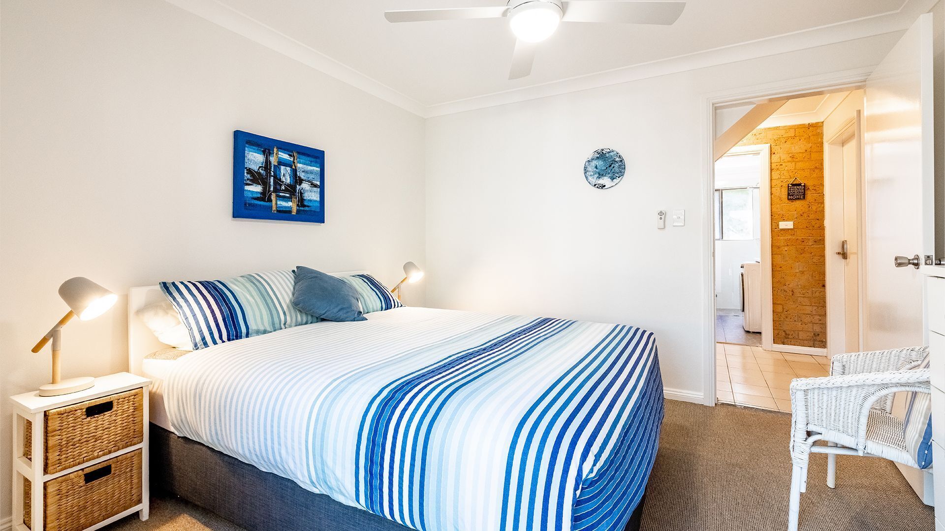 A bedroom with a bed, bedside lamps, a wall clock, and a door leading to another room.