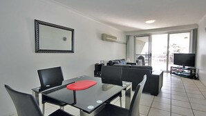 A modern living room with a dining area, a large window, and a flat-screen TV. - Nelson Towers, 9,71a Victoria Parade - unit in the heart of Nelson Bay with water views, air conditioning and Wi-Fi (Nelson Bay)