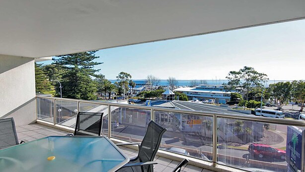 A balcony with a glass table and chairs, overlooking a parking area and a marina with boats. - Nelson Towers, 9,71a Victoria Parade - unit in the heart of Nelson Bay with water views, air conditioning and Wi-Fi (Nelson Bay)