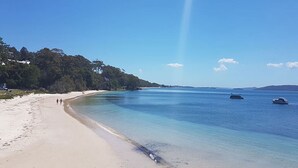 A beach with clear water, a sandy shore, and boats in the distance.
