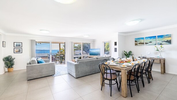 A spacious living area with a balcony overlooking a scenic view, a dining area with a wooden table and chairs, and a comfortable seating arrangement.