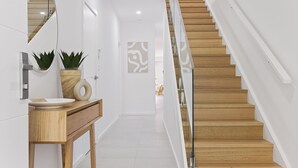 A modern interior with a wooden staircase, a white wall with a decorative panel, and a wooden vanity with a mirror and potted plants. - Hideaway 1, 3 Lillian St -  stunning water views (Shoal Bay)