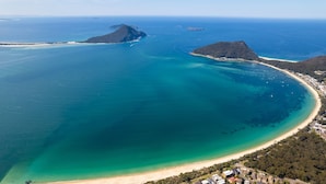 An aerial view of a coastal area with a large bay, a beach, and a small island. - Hideaway 1, 3 Lillian St -  stunning water views (Shoal Bay)