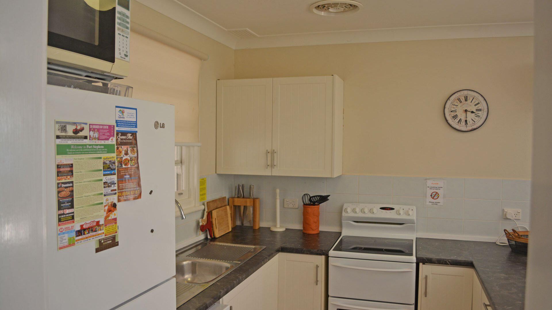 A kitchen with white cabinets, a stove, a sink, and a clock on the wall.