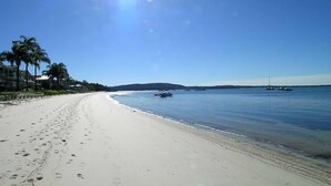Una playa con cielo despejado, agua tranquila y barcos.