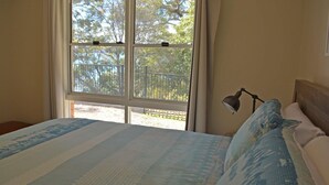 Un dormitorio con cama, mesita de noche, lámpara y ventana con vista a árboles.