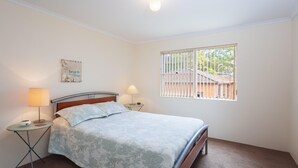 Een slaapkamer met een bed, twee nachtkastjes, een raam met zonwering en een bord aan de muur.