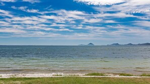 Uitzicht op de kust met rustig water, een grasachtige oever en verre eilanden onder een gedeeltelijk bewolkte lucht.