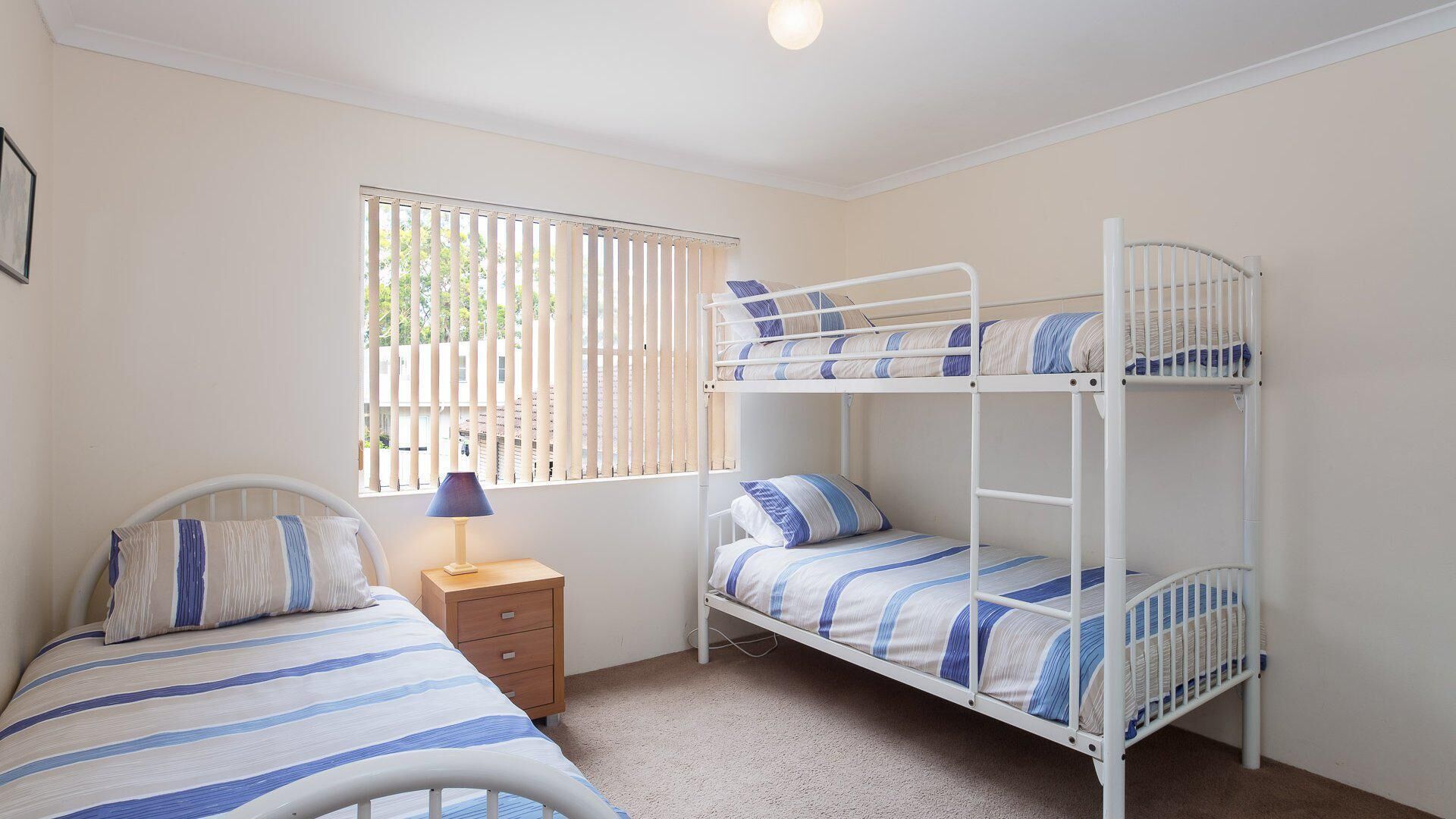 Habitación con literas, una ventana, una mesita de noche con lámpara y ropa de cama a rayas.
