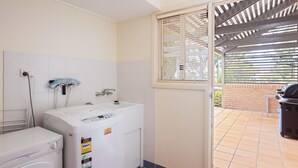 Een kleine badkamer met een wasmachine, een wastafel en een raam met zonwering.