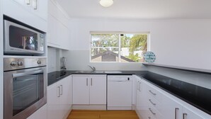 Een moderne keuken met witte kasten, een zwart aanrecht, een ingebouwde oven, een magnetron, een spoelbak en een raam met uitzicht op groen.
