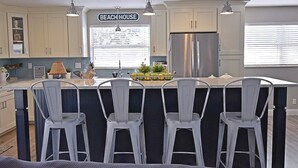Eine Küche mit einer großen Kochinsel, Barhocker, einem Kühlschrank und einem Schild mit der Aufschrift 'BEACH HOUSE'.