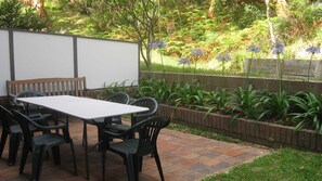 An outdoor patio with a table and chairs, surrounded by a garden with various plants and flowers. - Adriana, 4/83 Ronald Avenue - open plan living with backyard (Shoal Bay)
