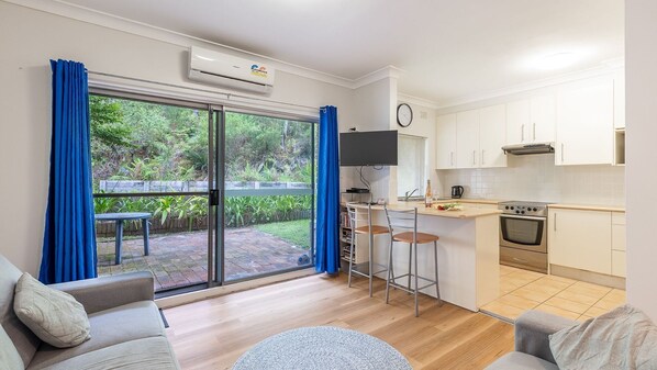 A modern apartment with a kitchen, dining area, and a large sliding glass door leading to a garden. - Adriana, 4/83 Ronald Avenue - open plan living with backyard (Shoal Bay)