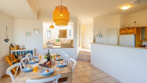 Un coin repas avec une table en bois dressée pour le repas, une cuisine avec des placards en bois et un salon avec un canapé et une table basse.