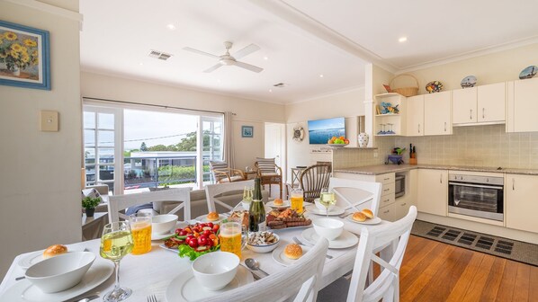 A modern kitchen with white cabinets, a dining area with a white table set for a meal, and a large window offering a view of the outdoors.