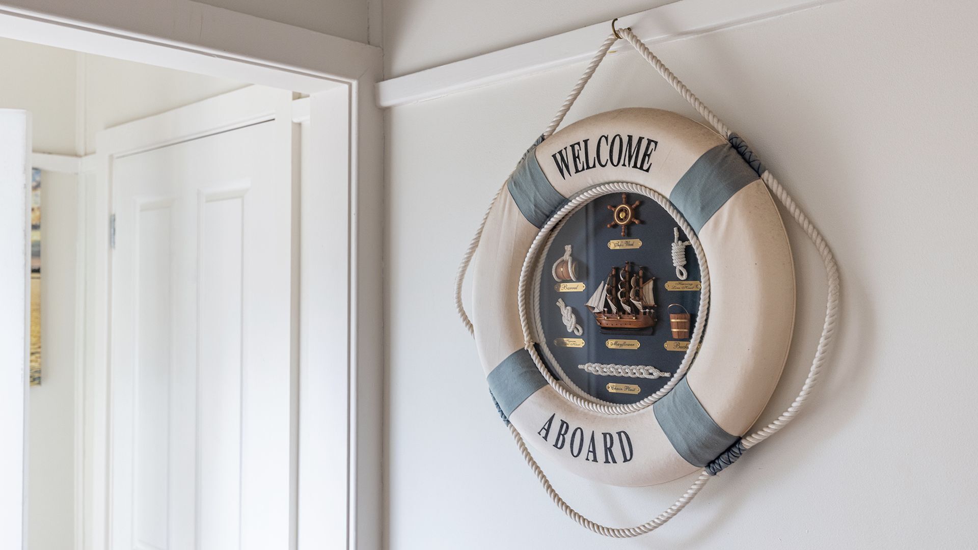 A life preserver wall hanging with nautical decorations and the words "WELCOME" and "ABORD" on a white door.