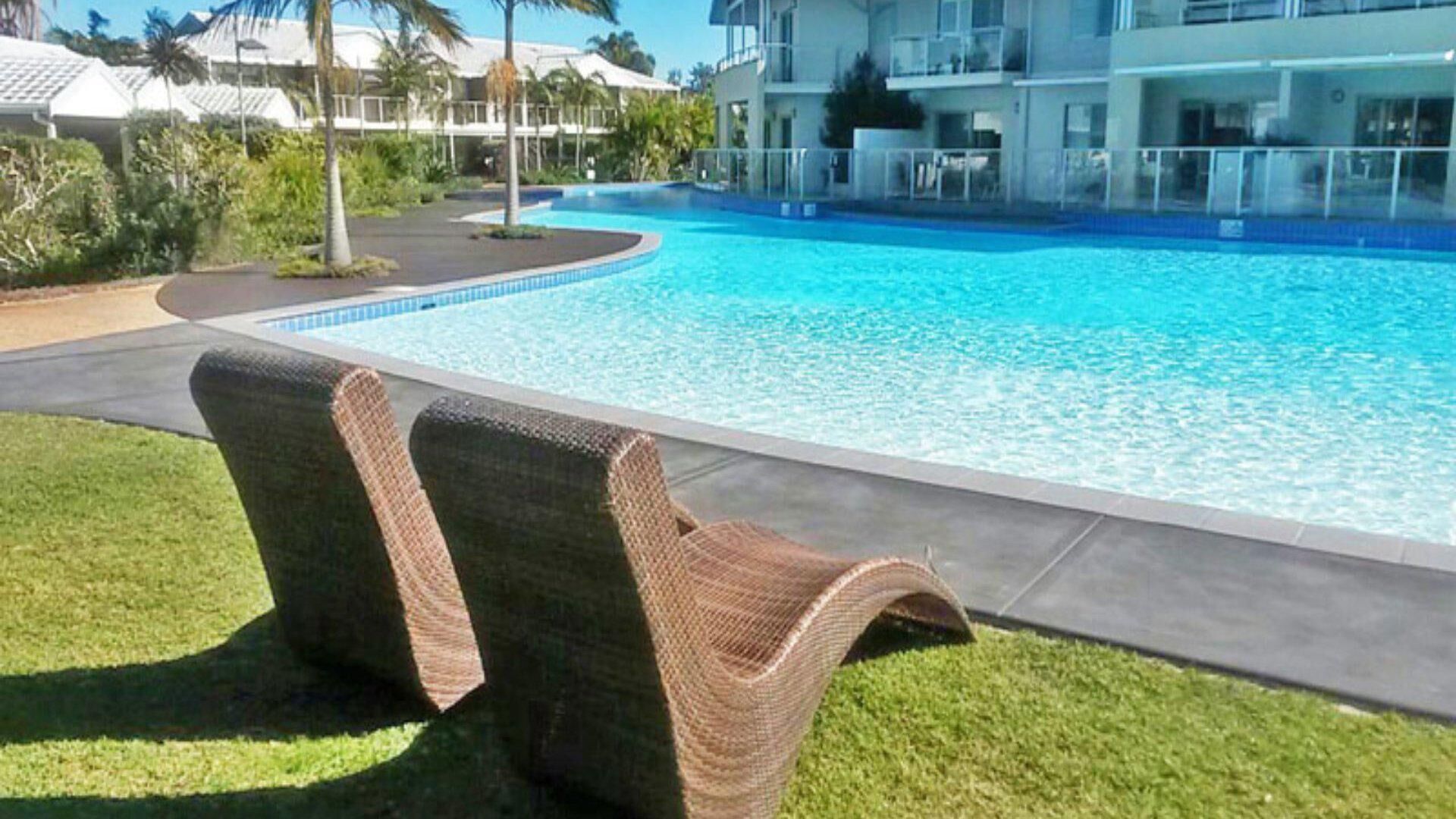 Una piscina con lettini, una zona verde e un edificio sullo sfondo.