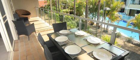 Un balcón con una mesa para cuatro, con vistas a una piscina y palmeras.