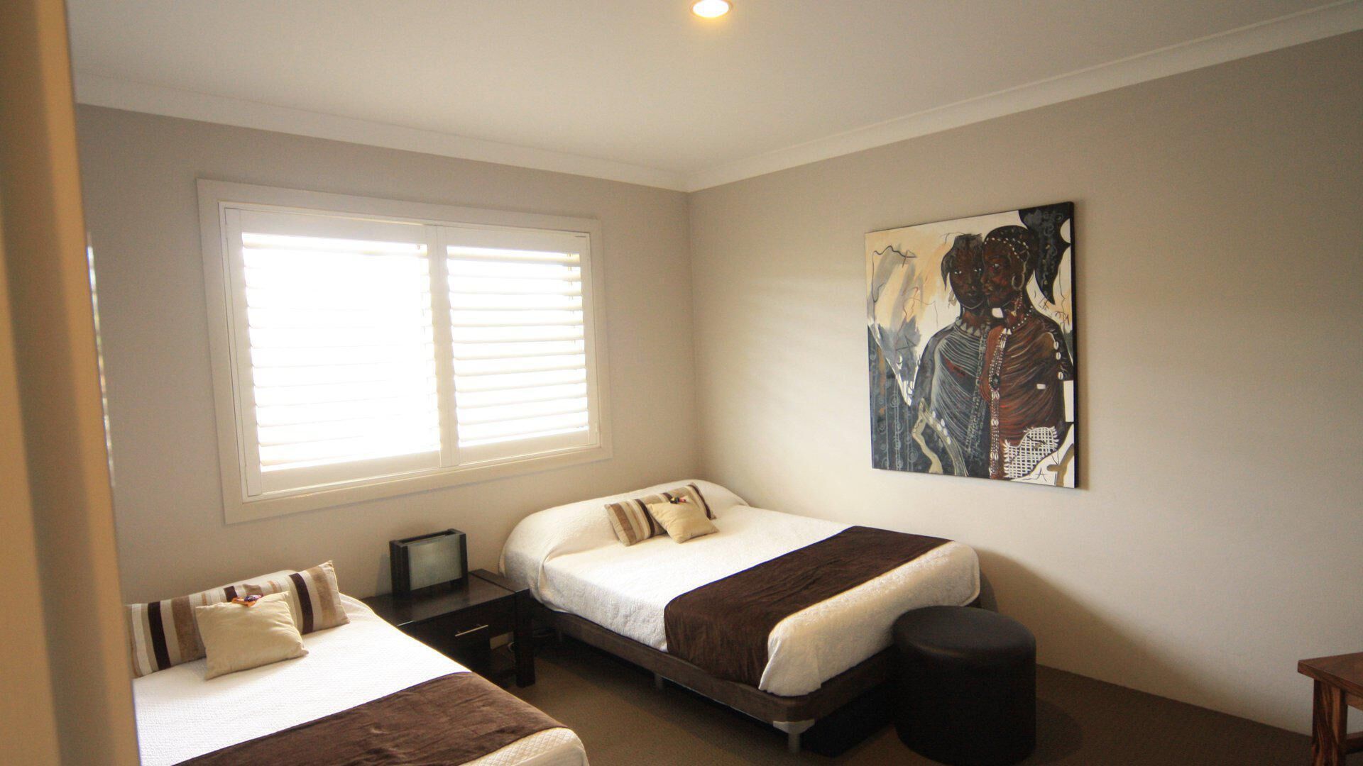 A bedroom with two beds, a large window, a painting on the wall, and a small table with a television.